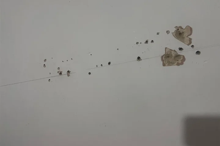 Multiple drill holes and wall damage left from a failed TV mounting attempt before repair.